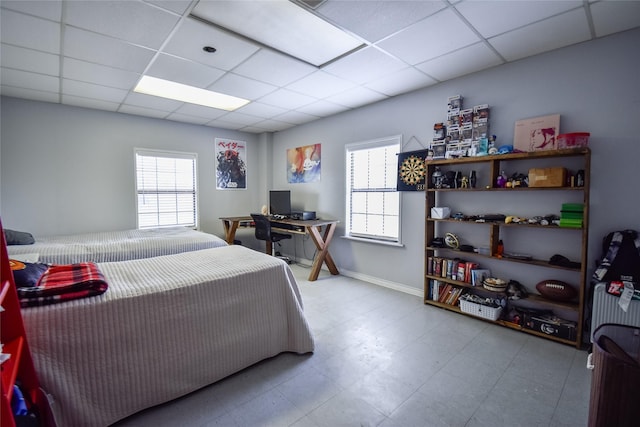 bedroom featuring light floors, a drop ceiling, and baseboards