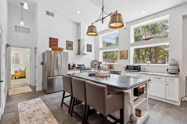 kitchen with appliances with stainless steel finishes, decorative light fixtures, wall chimney range hood, white cabinetry, and open shelves