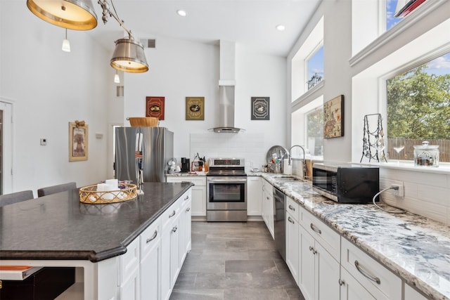 kitchen with a sink, visible vents, white cabinets, appliances with stainless steel finishes, and wall chimney exhaust hood