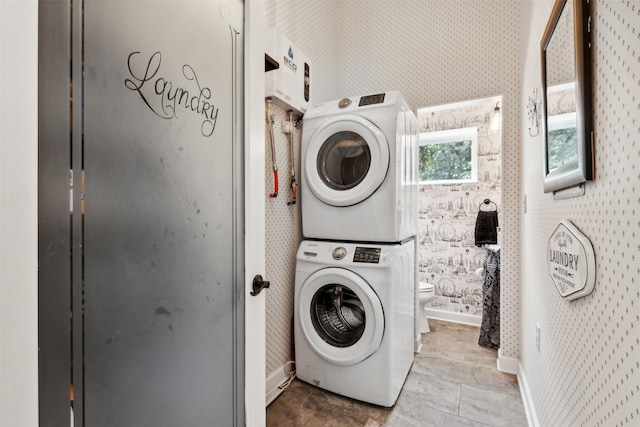 clothes washing area with laundry area, stacked washer / dryer, baseboards, stone finish flooring, and wallpapered walls