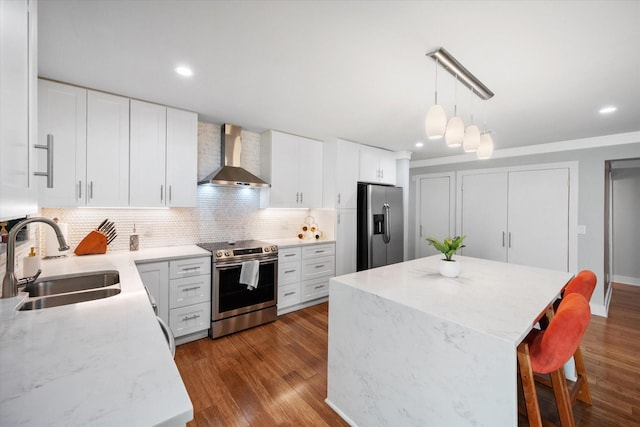 kitchen with a sink, white cabinets, appliances with stainless steel finishes, wall chimney exhaust hood, and decorative light fixtures