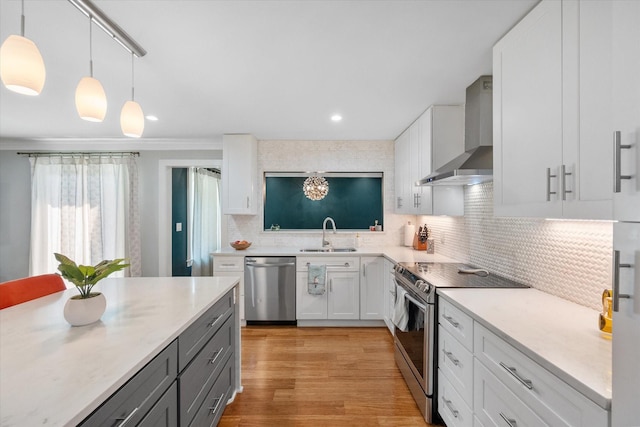 kitchen featuring decorative light fixtures, light countertops, appliances with stainless steel finishes, white cabinetry, and wall chimney range hood