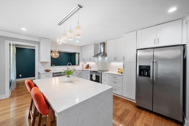 kitchen with decorative light fixtures, stainless steel appliances, tasteful backsplash, white cabinets, and wall chimney range hood