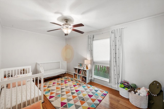 bedroom featuring a crib, wood finished floors, and a ceiling fan