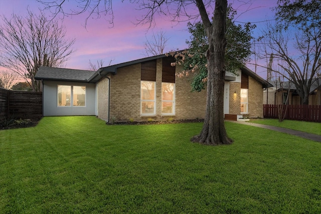 back of property at dusk featuring a yard, brick siding, and fence