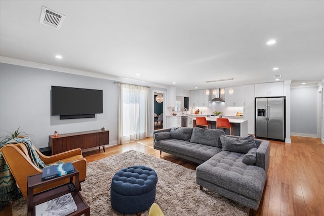 living room featuring baseboards, visible vents, crown molding, light wood-style floors, and recessed lighting