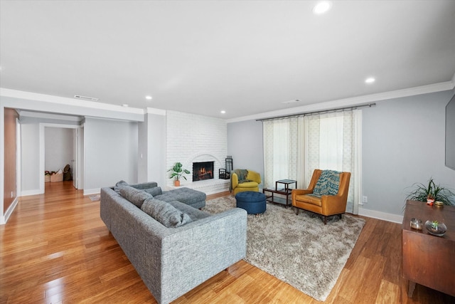 living area with a brick fireplace, visible vents, crown molding, and light wood-style flooring