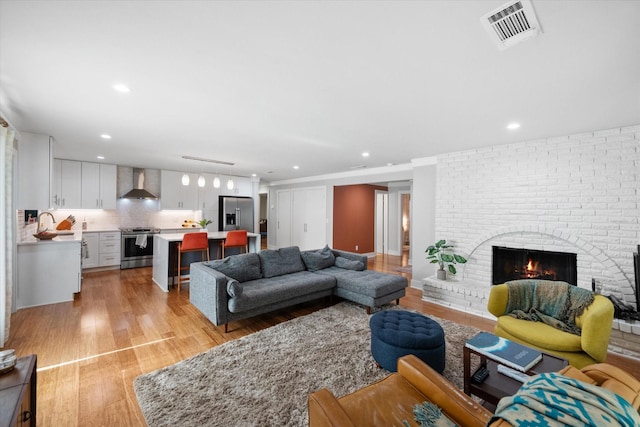 living room with recessed lighting, a brick fireplace, visible vents, and light wood finished floors