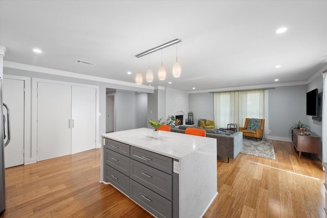 kitchen with pendant lighting, gray cabinetry, open floor plan, light wood-type flooring, and crown molding