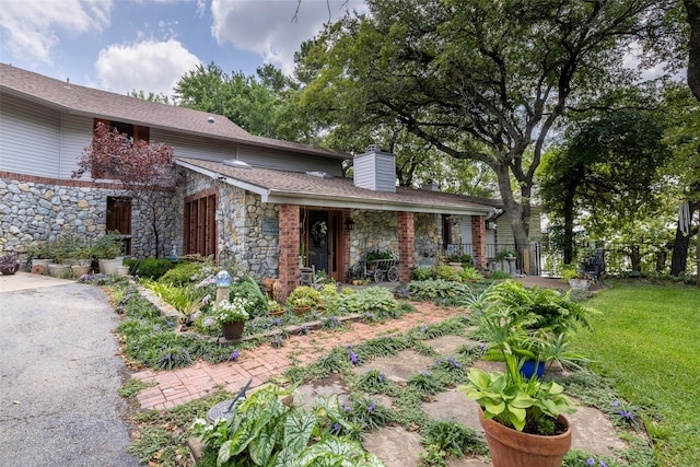 view of front of house with stone siding, a chimney, a front yard, and fence