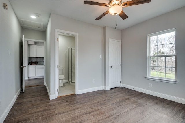 unfurnished bedroom with dark wood-style floors, ensuite bathroom, attic access, a ceiling fan, and baseboards