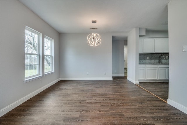 unfurnished dining area featuring visible vents, baseboards, dark wood-style flooring, a notable chandelier, and a sink