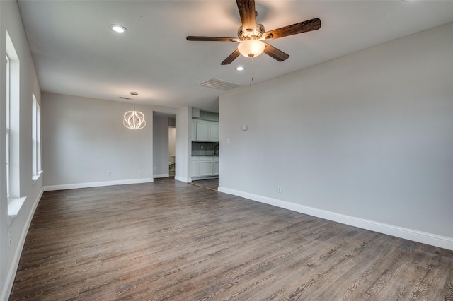 empty room featuring baseboards, visible vents, dark wood-type flooring, and ceiling fan with notable chandelier