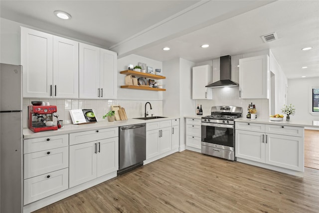 kitchen featuring open shelves, visible vents, appliances with stainless steel finishes, a sink, and wall chimney exhaust hood