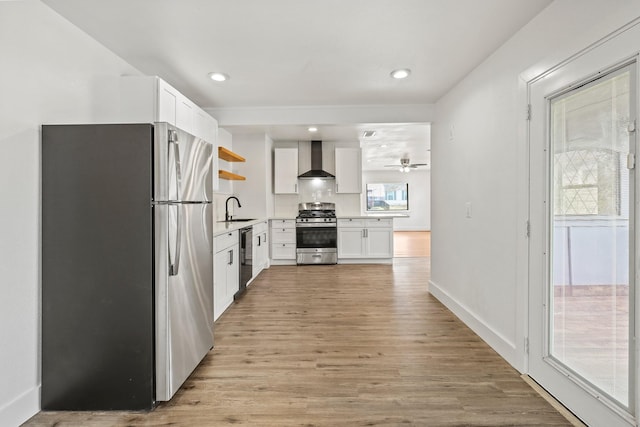 kitchen featuring stainless steel appliances, a sink, wall chimney exhaust hood, open shelves, and light wood finished floors