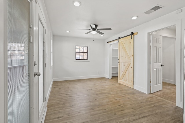 unfurnished room featuring a ceiling fan, visible vents, light wood finished floors, and a barn door