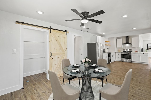 dining area with a barn door, baseboards, wood finished floors, and recessed lighting