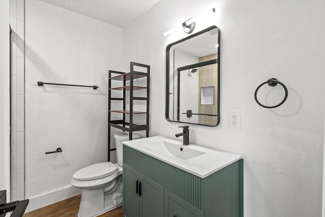 bathroom featuring a textured ceiling, toilet, wood finished floors, vanity, and a tile shower