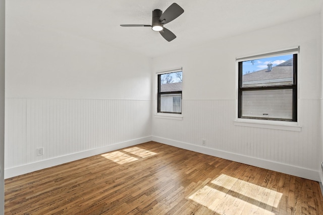 unfurnished room featuring a wainscoted wall, baseboards, hardwood / wood-style flooring, and a ceiling fan