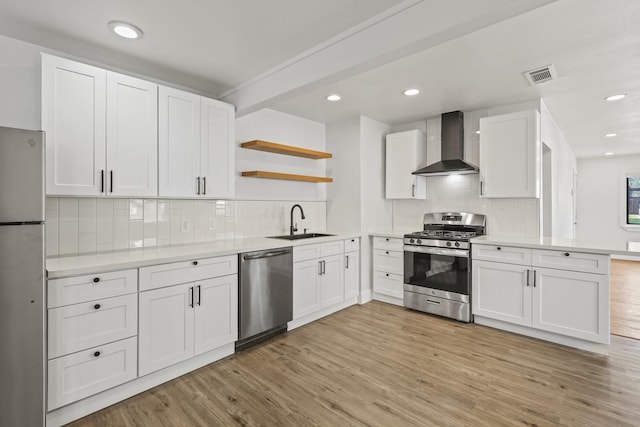 kitchen with appliances with stainless steel finishes, light wood-type flooring, wall chimney range hood, open shelves, and a sink