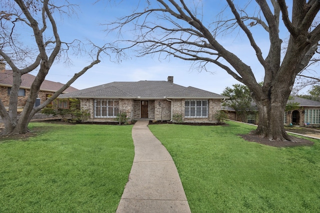 view of front of house with roof with shingles, brick siding, a front lawn, and a chimney