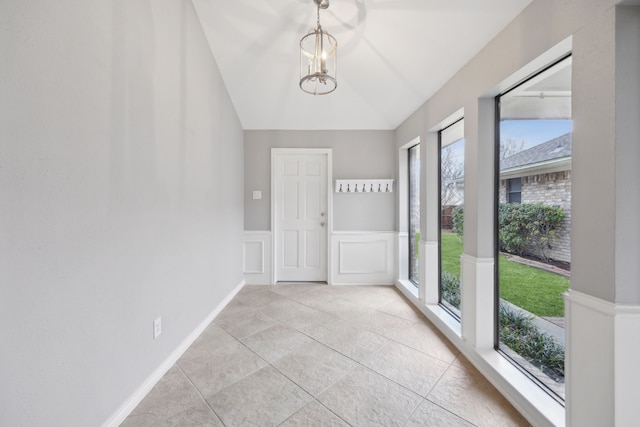 unfurnished room with a wainscoted wall, lofted ceiling, a decorative wall, light tile patterned flooring, and a chandelier