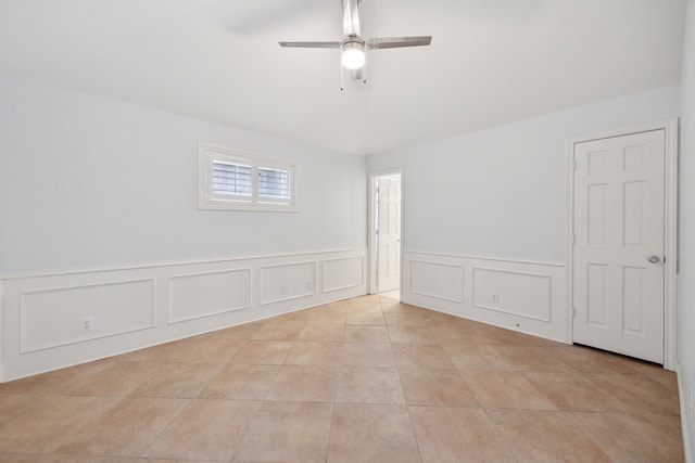 empty room featuring ceiling fan, light tile patterned flooring, and a decorative wall