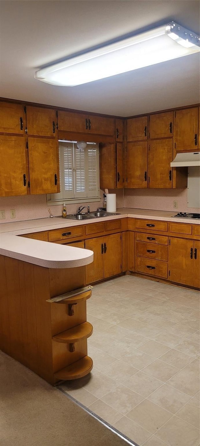 kitchen with under cabinet range hood, brown cabinets, light countertops, and black electric cooktop