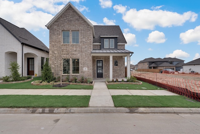 view of front of house with a shingled roof, metal roof, a standing seam roof, a front lawn, and brick siding