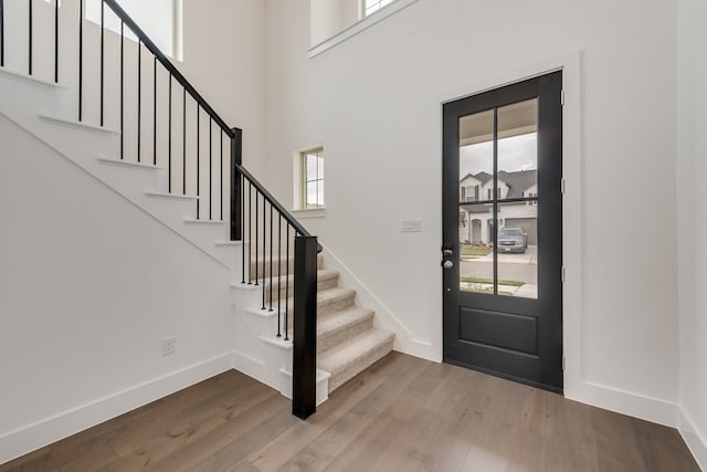 entryway with stairway, wood finished floors, a towering ceiling, and baseboards