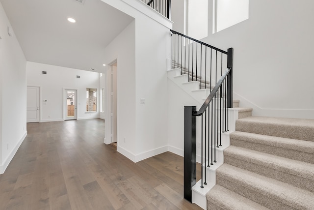 staircase featuring a high ceiling, recessed lighting, wood finished floors, and baseboards