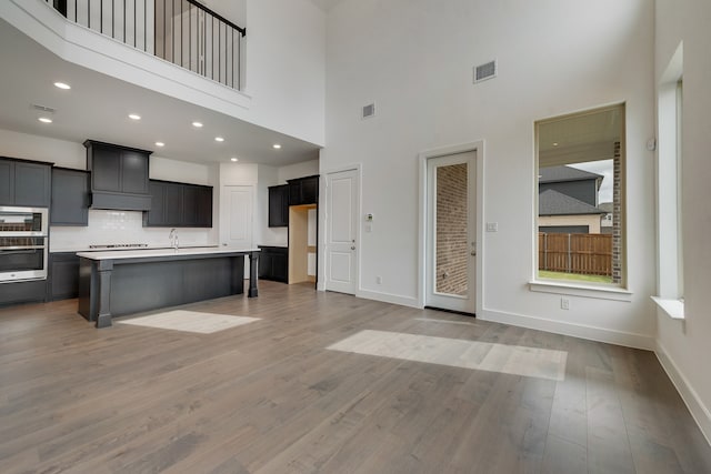 kitchen featuring a center island with sink, light countertops, visible vents, open floor plan, and wood finished floors