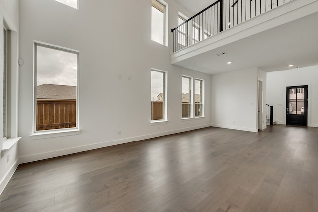 unfurnished living room with visible vents, dark wood finished floors, a towering ceiling, and baseboards