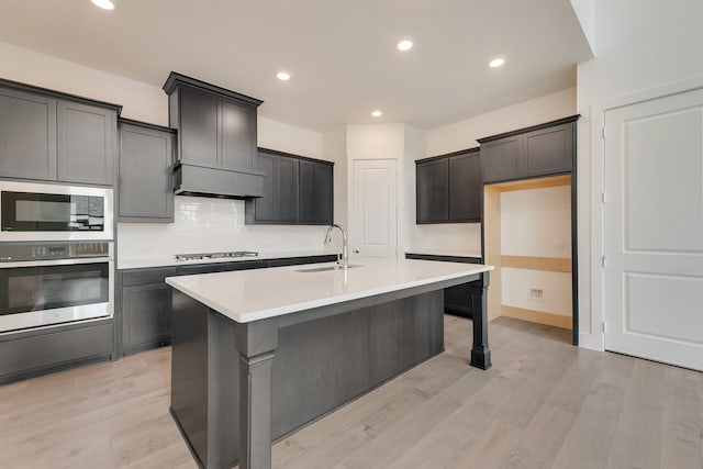 kitchen featuring a sink, light countertops, appliances with stainless steel finishes, light wood finished floors, and a center island with sink