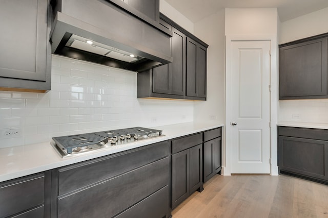 kitchen featuring light wood finished floors, tasteful backsplash, light countertops, stainless steel gas stovetop, and wall chimney range hood