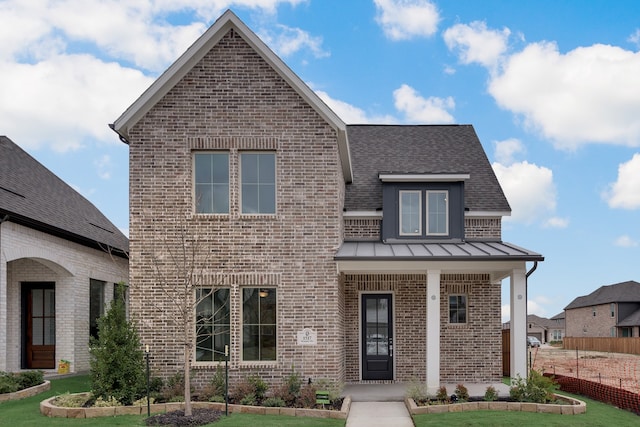 view of front of home featuring a standing seam roof, a front lawn, covered porch, and brick siding