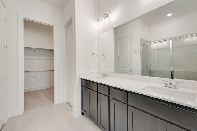 bathroom featuring double vanity, a stall shower, a spacious closet, and a sink