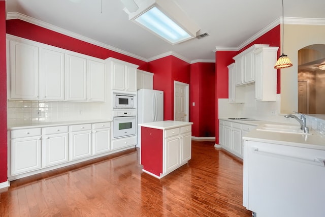 kitchen with white appliances, a sink, a kitchen island, light countertops, and hanging light fixtures