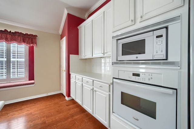 kitchen with white appliances, ornamental molding, wood finished floors, light countertops, and white cabinetry