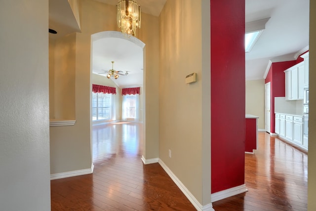 hall featuring vaulted ceiling, hardwood / wood-style floors, arched walkways, and baseboards