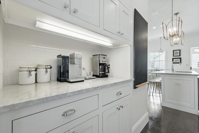 kitchen featuring light stone counters, decorative light fixtures, decorative backsplash, white cabinets, and a sink