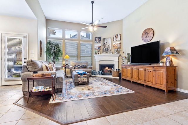 living room with a ceiling fan, plenty of natural light, a lit fireplace, and wood finished floors