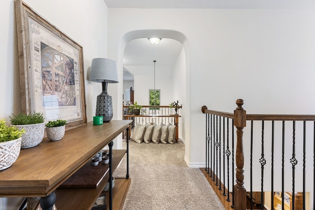 hall with arched walkways, carpet, an upstairs landing, and baseboards