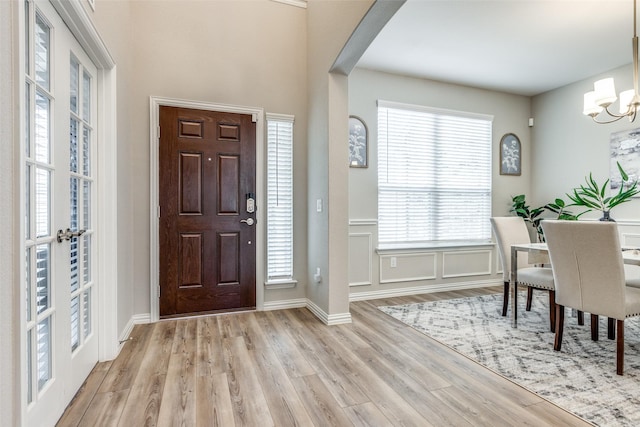 entryway with arched walkways, french doors, a decorative wall, an inviting chandelier, and light wood-type flooring