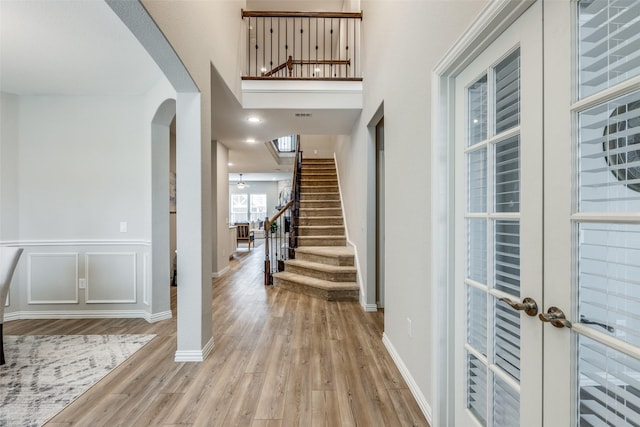 foyer entrance featuring arched walkways, stairs, french doors, light wood-style floors, and a decorative wall