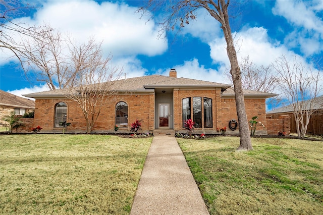 ranch-style house featuring roof with shingles, a chimney, a front lawn, and brick siding