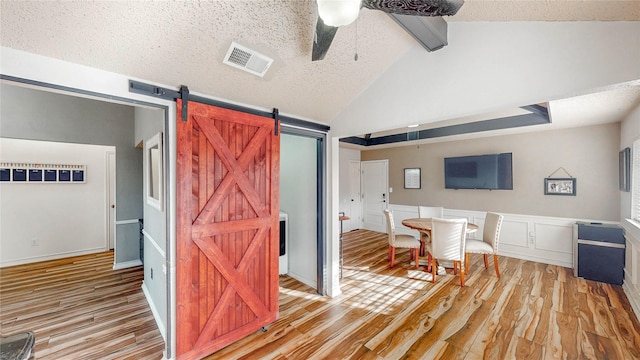 dining space featuring vaulted ceiling with beams, ceiling fan, a textured ceiling, visible vents, and light wood-type flooring