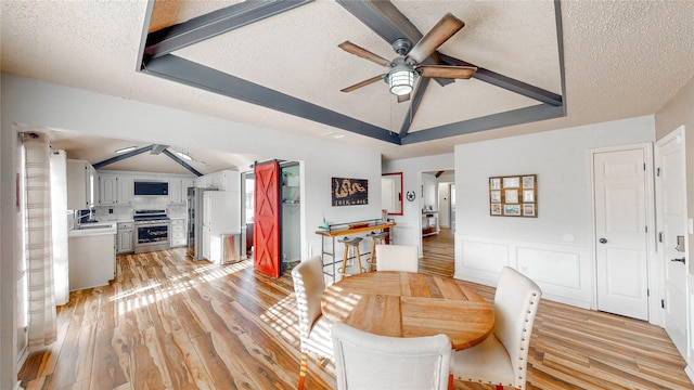 dining room with a textured ceiling, a ceiling fan, vaulted ceiling, light wood finished floors, and a raised ceiling