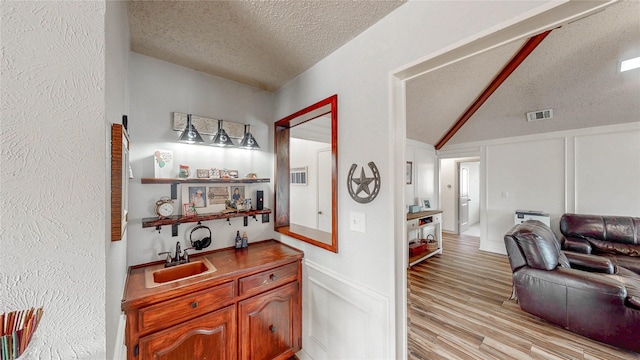 bar featuring lofted ceiling, a textured ceiling, a decorative wall, a sink, and wet bar