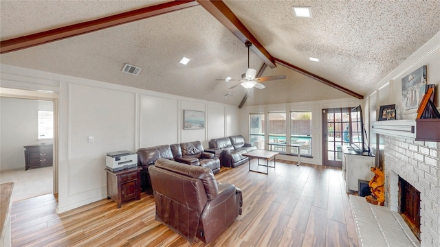 living area featuring lofted ceiling with beams, a decorative wall, a fireplace, visible vents, and light wood-type flooring